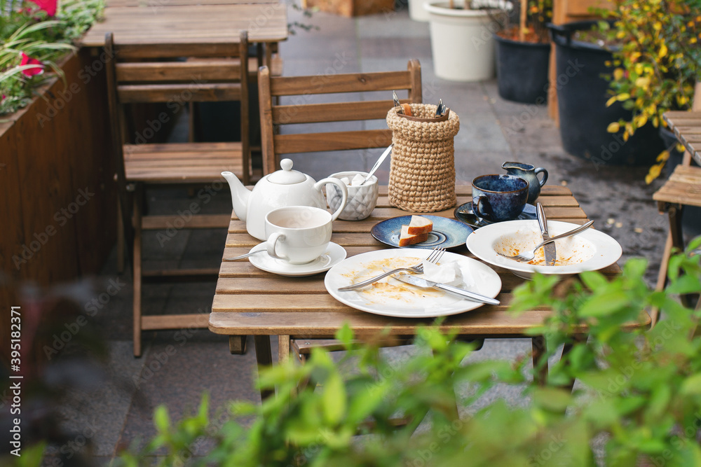 dirty white dishes on wooden table with cutlery in cafe on street without people dirty white dishes on wooden table with cutlery in cafe on street without people