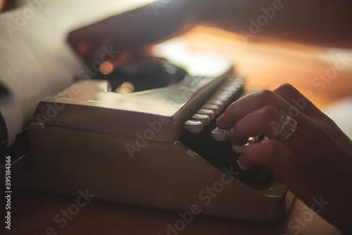 Process of writing a text letter on a white sheet of paper with old-fashioned typewriter, modern writer machine in warm room light, close up view of hands writing and printing