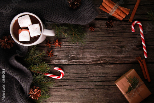 Cocoa with marshmallow, cinnamon, knitted scarf, fir tree branches, cones, craft gift box, candy cane on rustic wooden table. Winter and Christmas concept. Hot drink, New Year, top view, copy space