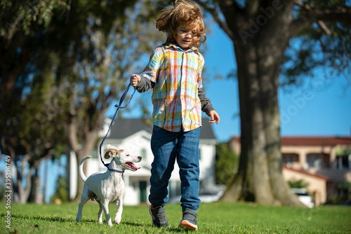 Child and puppy outside. Happy Kid boy and dog running at backyard lawn. Pet walking.