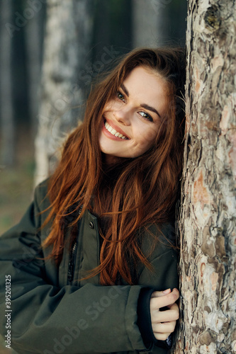 Smiling women in a jacket near a tree in the forest