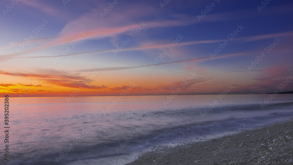 After sunset. Dusk. The blue sky is highlighted in orange, traces of flying planes. Reflection on the surface of the sea. A wave rolls on the pebble beach.