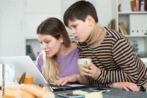 Portrait of young woman and son chatting at table with laptop indoors