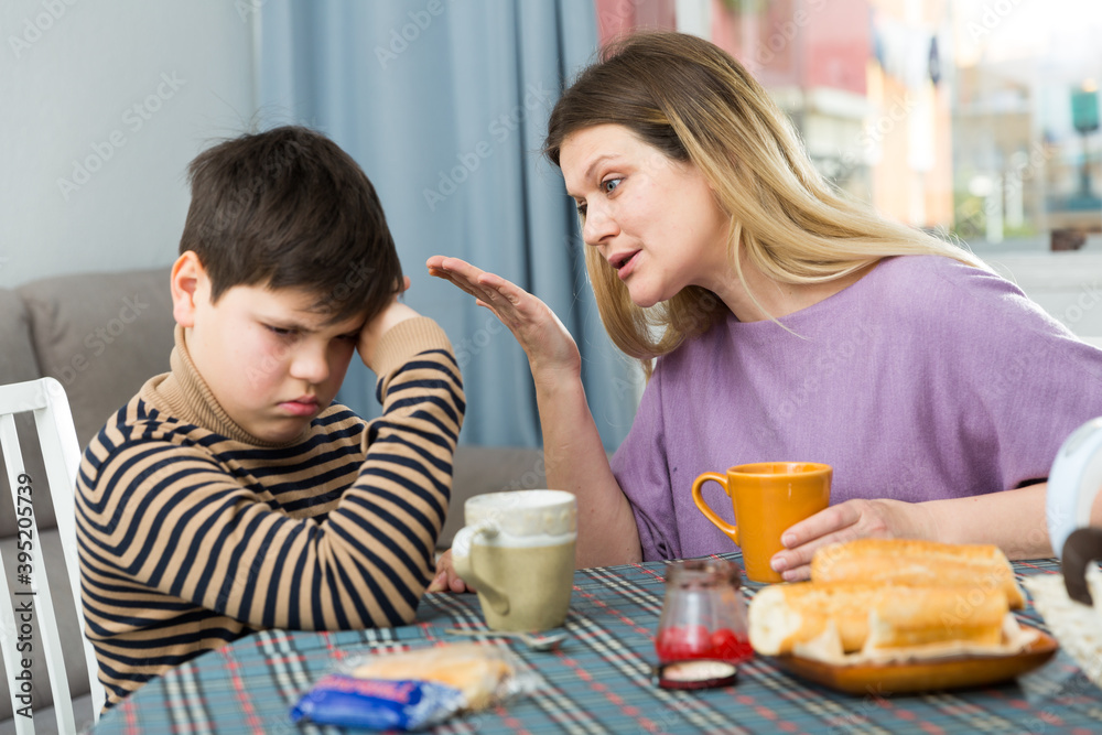 Upset mother and unhappy son arguing during breakfast in domestic interior