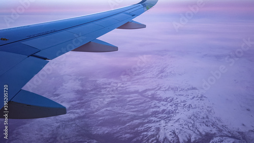 Air plane flies among the clouds over snowy capped mountains.