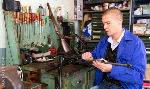 Male gunsmith repairing hunting rifle in a workshop photo