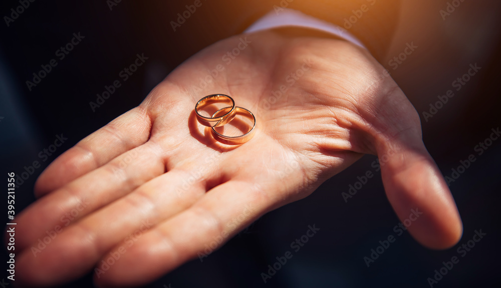 Two crossed wedding rings on the groom's palm top view, close-up. Gold rings in a man's hand in the sunlight. Wedding day, celebration. Two crossed wedding rings on the groom's palm top view, close-up. Gold rings in a man's hand in the sunlight. Wedding day, celebration.