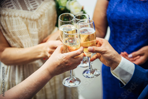 Guests and relatives of different ages at the wedding raise their glasses with festive champagne. Hands with drinks close-up. Marriage celebration, congratulations.