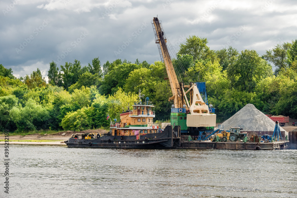 Crane and barge for sand on shore of Volga river at spring cloudy day Crane and barge for sand on shore of Volga river at spring cloudy day