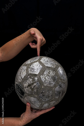 Old soccer ball in the hands of a teenager on a black background.