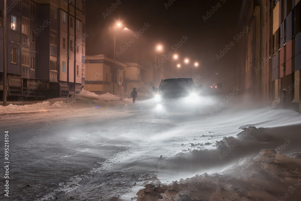 Night winter view of a snow-covered street in a northern city in the Arctic. The car is driving on a snowy road. Cold winter weather. Bad visibility. Harsh polar climate. Anadyr, Chukotka, Russia. Night winter view of a snow-covered street in a northern city in the Arctic. The car is driving on a snowy road. Cold winter weather. Bad visibility. Harsh polar climate. Anadyr, Chukotka, Russia.