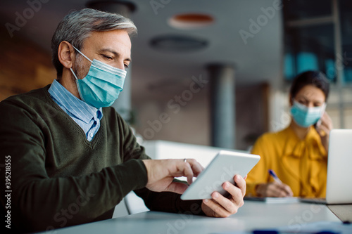 Male entrepreneur with face mask using digital tablet while working in the office.