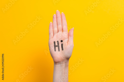World hello day. Raised female hand with the inscription Hi on the palm. Yellow background. Copy space
