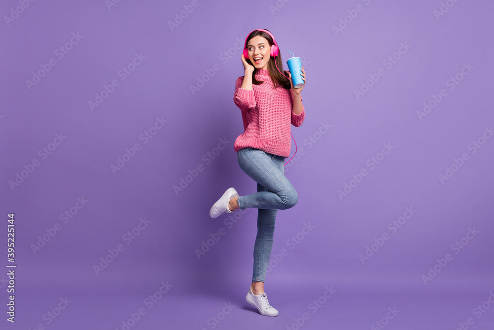 Full length body size photo of young woman listening music earphones smiling keeping cup of soda isolated on bright purple color background