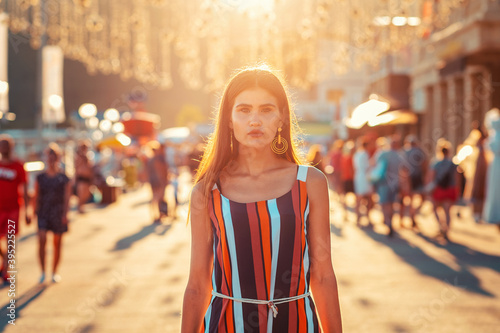 Portrait of a tanned woman in dress walking down the street.In the background, the sunset light and people in a blur. Concept of social advertising, business and psychology