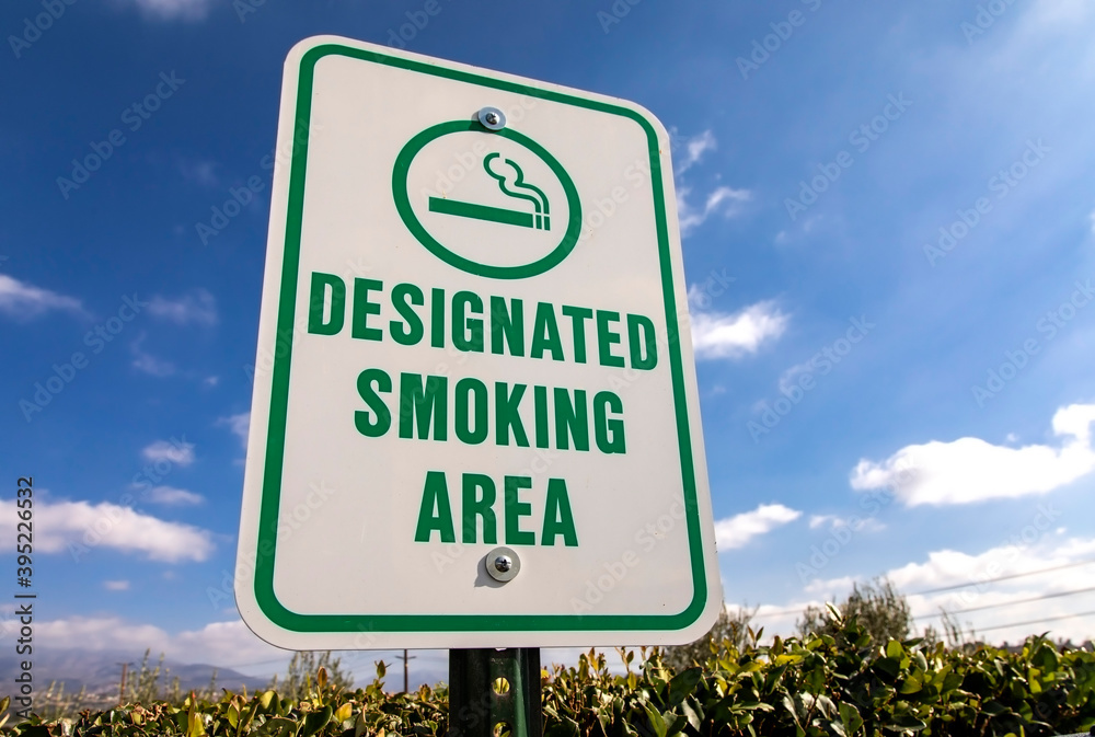A sign designating a cigarette smoking area against a blue sky and cloud Background