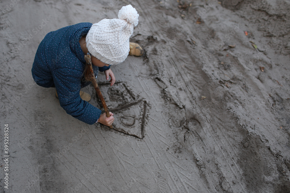 Child draws with a stick a house on the sand in the woods outdoors