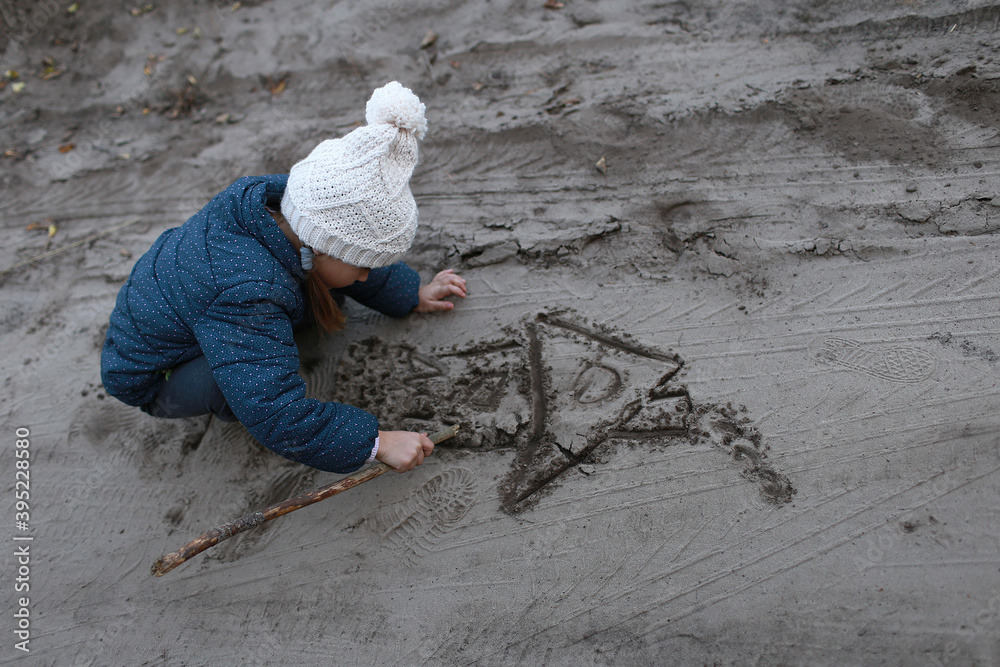 Child draws with a stick a house on the sand in the woods outdoors Child draws with a stick a house on the sand in the woods outdoors