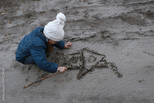 Child draws with a stick a house on the sand in the woods outdoors