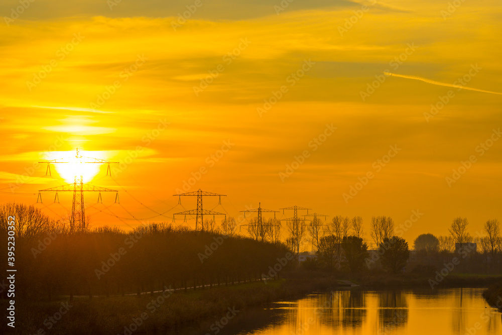 Trees in fall colors along a canal under a yellow cloudy sky at sunset in autumn, Almere, Flevoland, The Netherlands, November 24, 2020