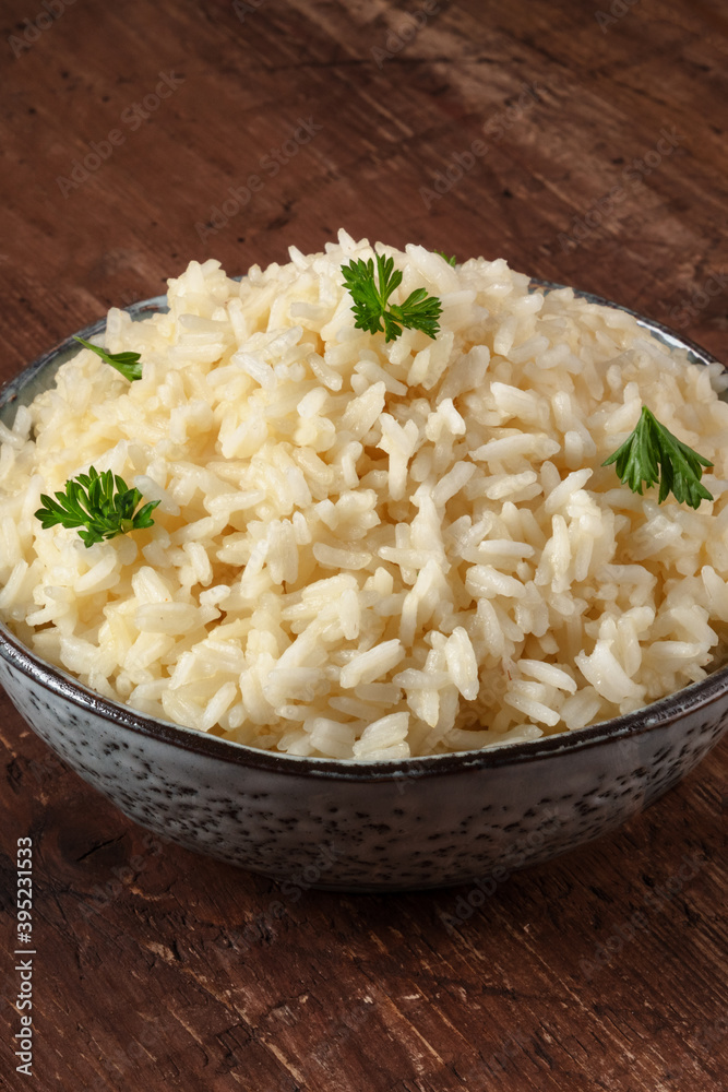 Cooked rice in a bowl, close-up on a wooden table, served with parsley leaves