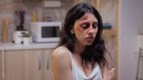 Beaten woman siting on the chair pushed by violent husband. Traumatised abused terrified beaten wife covered in bruises suffering injury from alcoholic aggressive brutal drunk man.