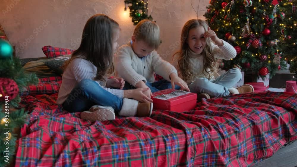 Children open a New Year's gift and are surprised. Joyful and cheerful children near the Christmas tree. Children open a New Year's gift and are surprised. Joyful and cheerful children near the Christmas tree.