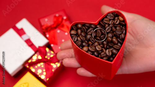 Top view woman hold hand colorful box gifts presents bright isolated on red background with roasted coffee beans. Concept Valentine's Day. Love symbol, heart shape. Brown shiny whole grains © Volodymyr