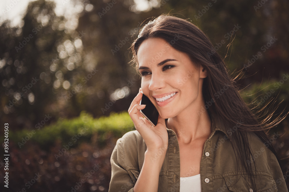 Photo of charming inspired young lady look side hold smartphone listen communicate wear brown shirt park street outside Photo of charming inspired young lady look side hold smartphone listen communicate wear brown shirt park street outside
