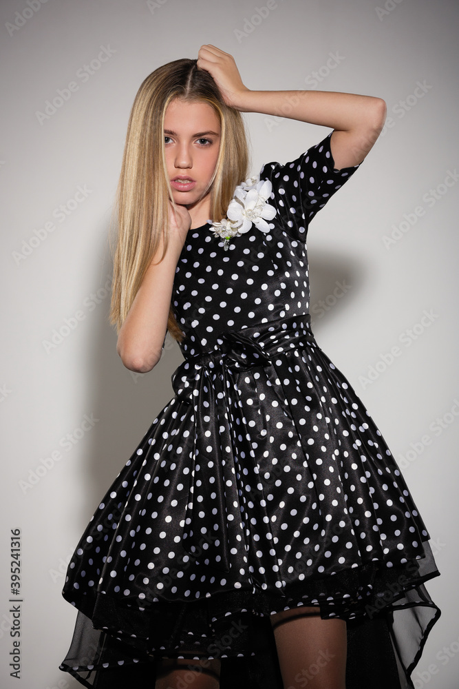 beautiful girl blonde teenager in a stylish black dress dress with white polka dots posing in the studio beautiful girl blonde teenager in a stylish black dress dress with white polka dots posing in the studio