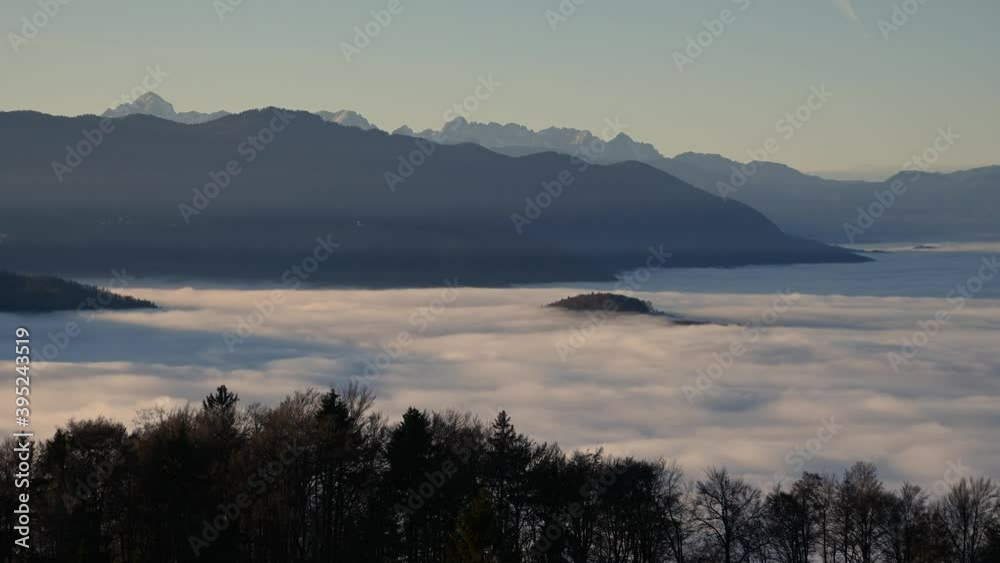 Time lapse elevated view above inversion clouds rolling in Alpine valley, Slovenia. Julian Alps in the distance. Colorful autumn sunset. Static shot, wide angle Time lapse elevated view above inversion clouds rolling in Alpine valley, Slovenia. Julian Alps in the distance. Colorful autumn sunset. Static shot, wide angle