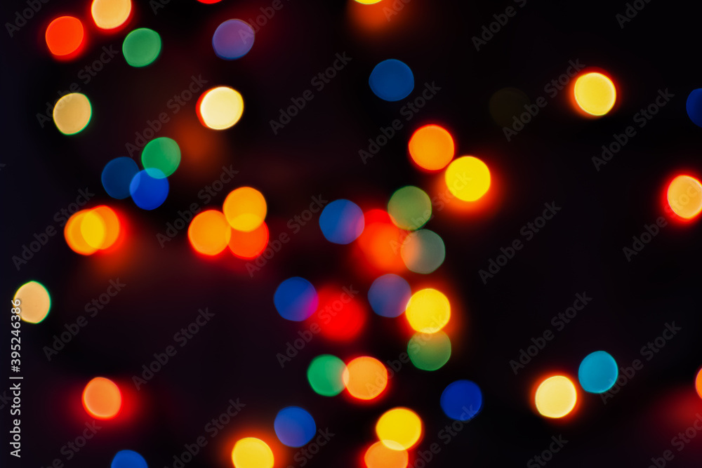 Multi-colored bokeh on a black background. Bright blurry textures of holiday lights. Colorful beautiful Christmas garlands on blurry background. Layout of a greeting card for the New year. Copy space