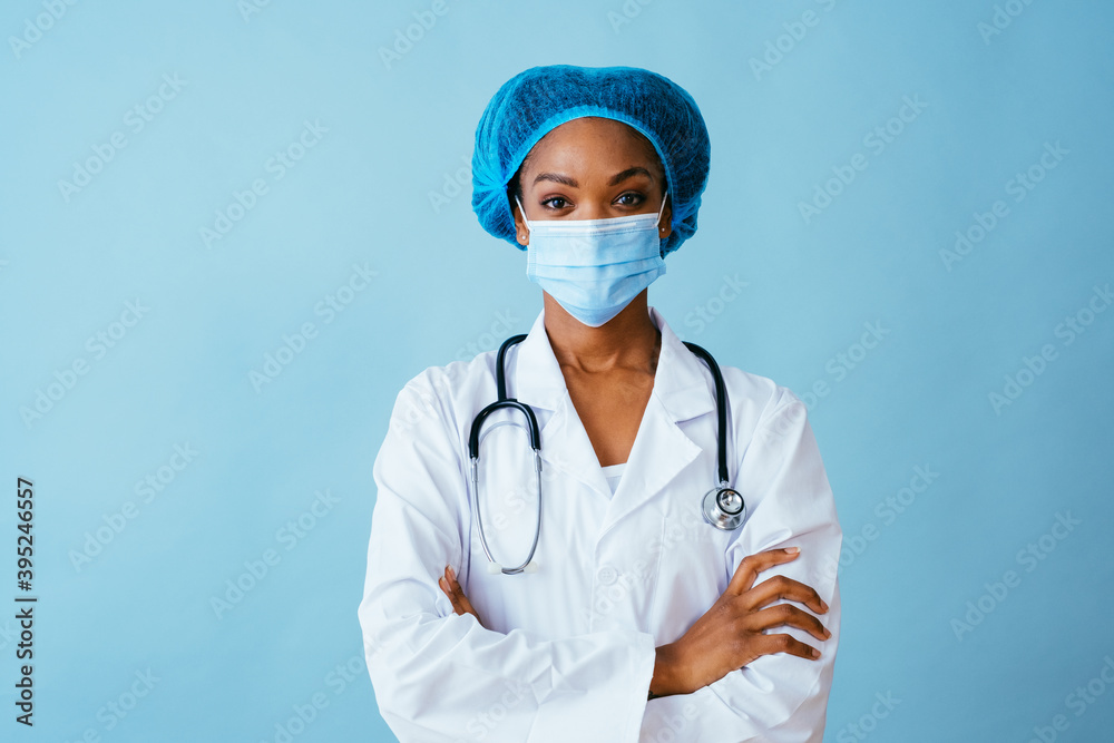 Portrait of a doctor in lab coat with face mask and hair protection with arms crossed, isolated on blue background Portrait of a doctor in lab coat with face mask and hair protection with arms crossed, isolated on blue background