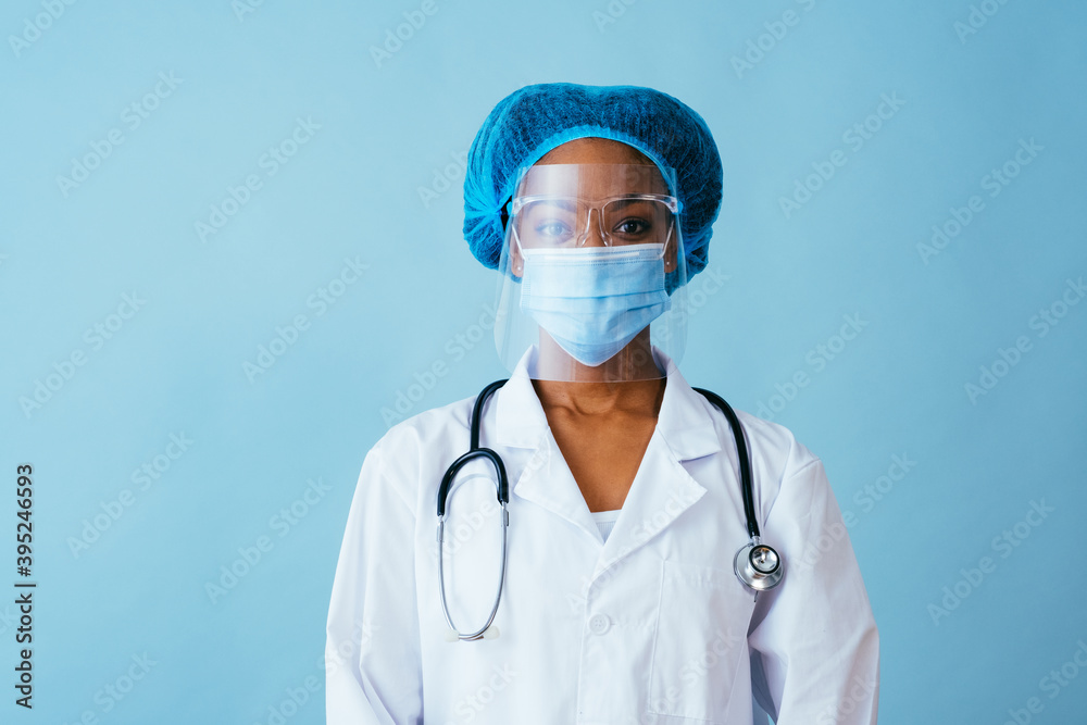 Portrait of a doctor in lab coat with face mask, face shield, and hair ppe isolated on blue Portrait of a doctor in lab coat with face mask, face shield, and hair ppe isolated on blue