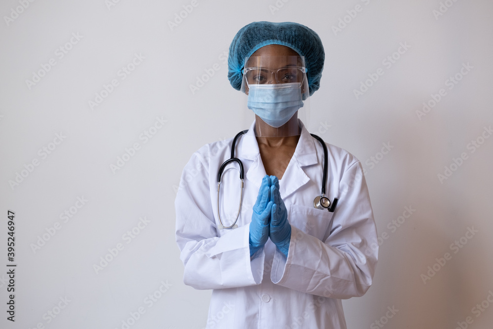 Portrait of a doctor in lab coat with face mask, face shield, and hair ppe with gloved hands together as if saying please or praying Portrait of a doctor in lab coat with face mask, face shield, and hair ppe with gloved hands together as if saying please or praying