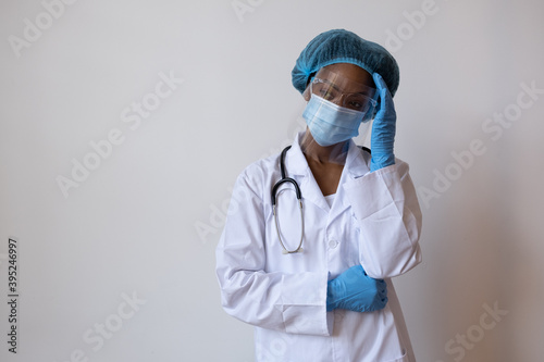 Portrait of a doctor in lab coat with face mask, face shield, and hair ppe holding head due to headache or problem