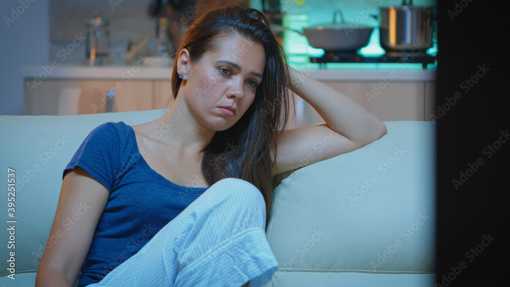 Tired woman closing eyes while watching movie at night. Tired exhausted lonely sleepy housewife in pajamas sleeping in front of television sitting on cozy couch in living room at home.