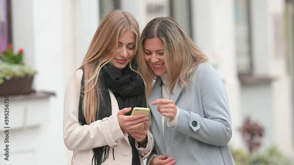 Portrait of happy Two female friends Using Mobile Phone outdoor. Smiling girl holding cellphone in hands outside. Communication, social networks, shopping concept. Portrait of happy Two female friends Using Mobile Phone outdoor. Smiling girl holding cellphone in hands outside. Communication, social networks, shopping concept.