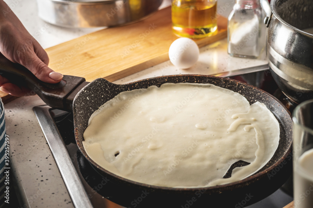 Person is standing at the stove and frying pancakes in a pan. Concept of the process of making a tasty breakfast at home Person is standing at the stove and frying pancakes in a pan. Concept of the process of making a tasty breakfast at home