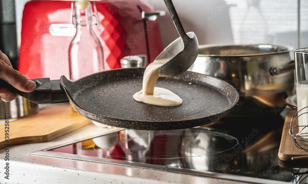 Person pouring the dough into a hot pan and frying homemade pancakes. Concept of making pancakes in your own kitchen Person pouring the dough into a hot pan and frying homemade pancakes. Concept of making pancakes in your own kitchen