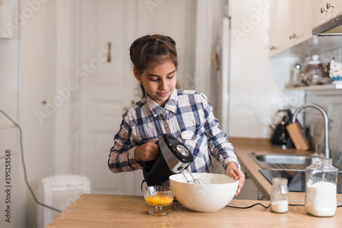 Little girl use a mixer to make a cake, skilled girl in kitchen. Child trying making cookies.
