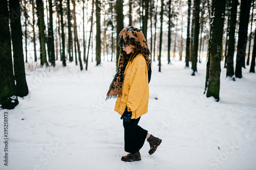 Funny strange young hipster girl with glasses and the scarf covering the head walking in the snow forest