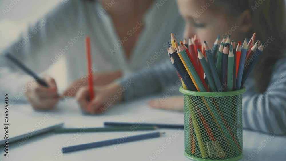 Colored pencils close-up. Young woman helps little girl to do homework. Colored pencils close-up. Young woman helps little girl to do homework.
