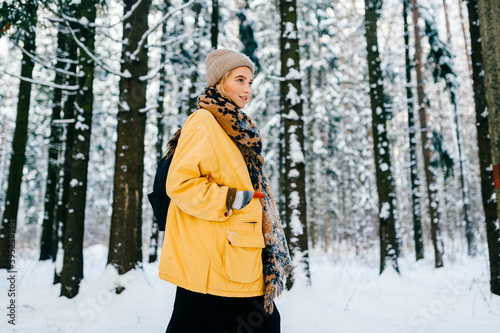 Young stylish hipster girl in yellow jacket with a warm scarf posing in the snow forest