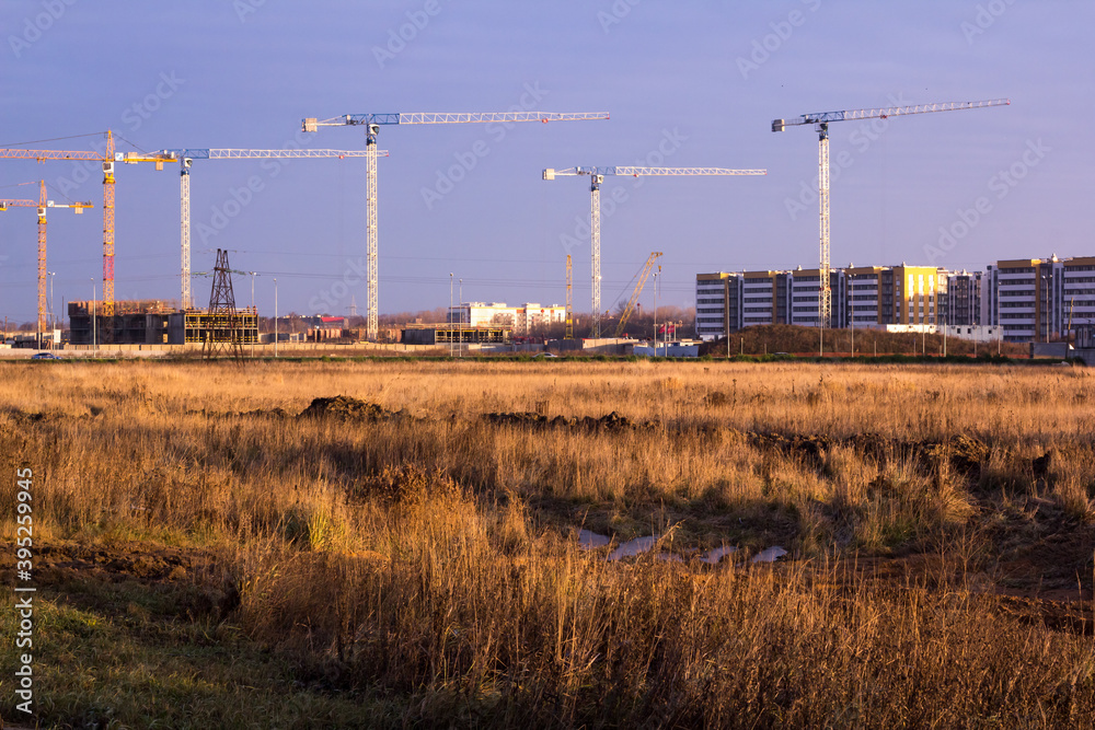 construction site with tower cranes in a field against a dark blue sky