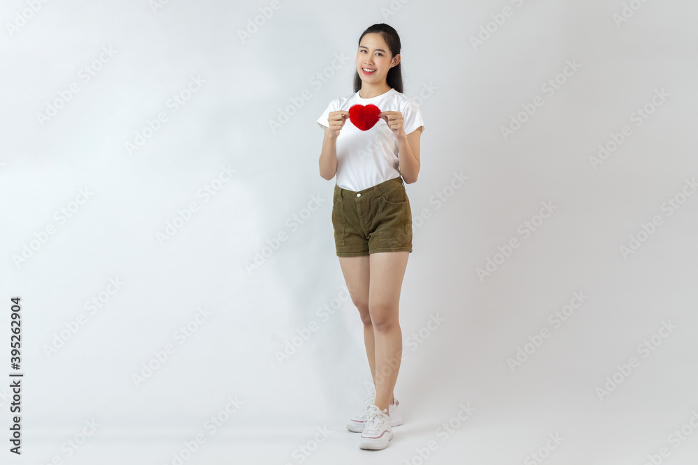 asian woman wearing white t-shirt and brown short pants with sneaker holding red heart standing on the white background asian woman wearing white t-shirt and brown short pants with sneaker holding red heart standing on the white background