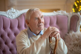 Grey-haired elderly man sitting on the sofa and looking aside
