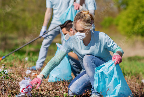 volunteering, health and ecology concept - group of volunteers wearing face protective medical masks for protection from virus disease with garbage bags cleaning area in park