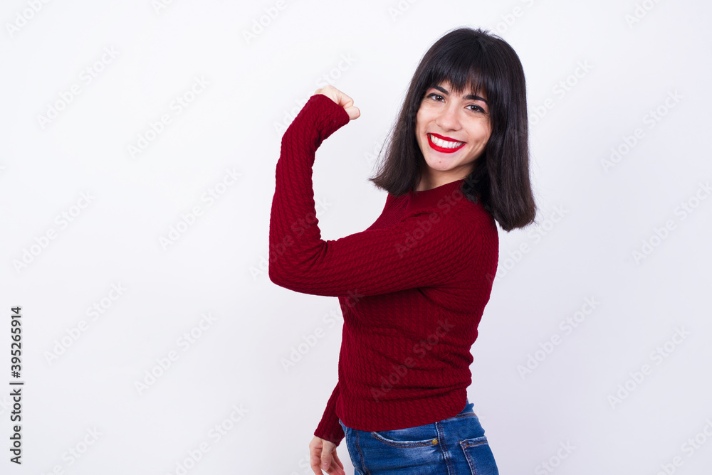 Young beautiful Caucasian woman wearing red T-shirt against white wall, showing muscles after workout. Health and strength concept. Young beautiful Caucasian woman wearing red T-shirt against white wall, showing muscles after workout. Health and strength concept.