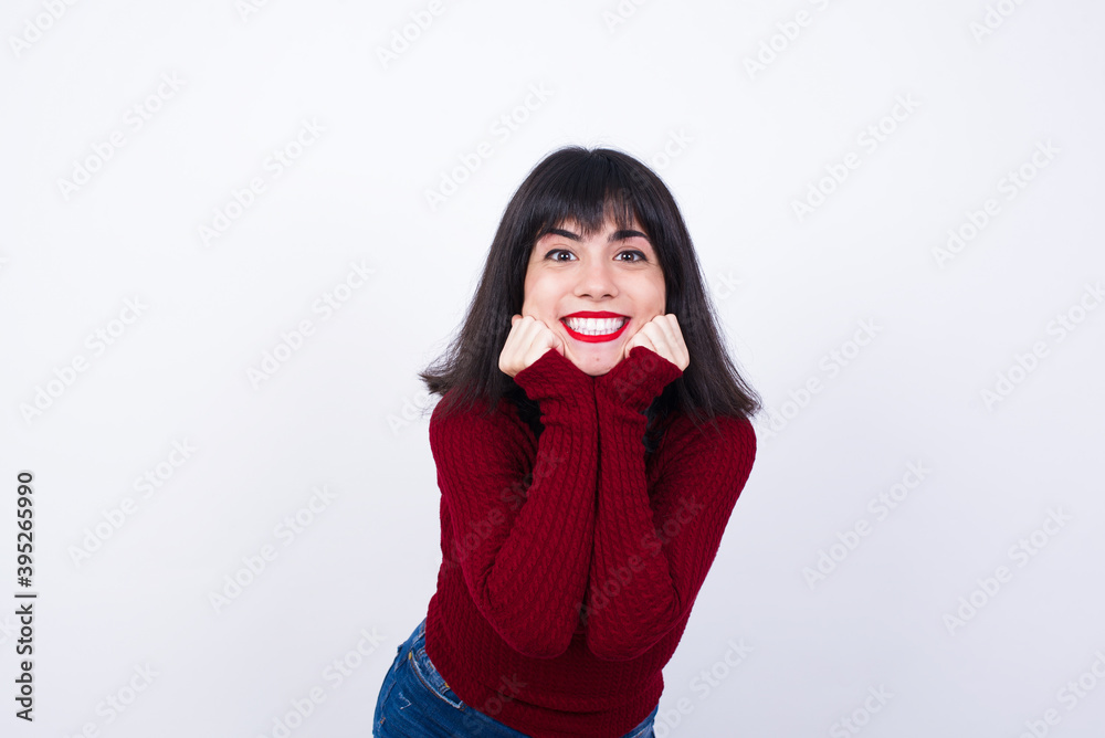 Dreamy Young beautiful Caucasian woman wearing red T-shirt against white wall, keeps hands pressed together under chin, looks with happy expression, has toothy smile. Dreamy Young beautiful Caucasian woman wearing red T-shirt against white wall, keeps hands pressed together under chin, looks with happy expression, has toothy smile.